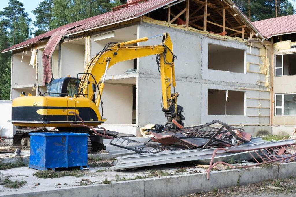 A yellow excavator demolishing an old house and removing it
